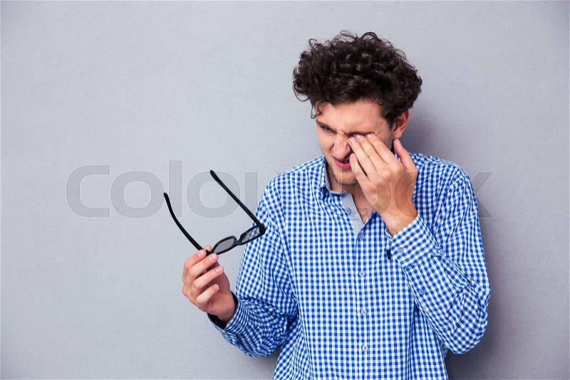 Man holding sunglasses and rubbing his eyes over gray background, stock photo
