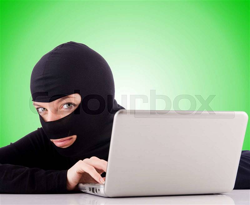 Hacker with computer wearing balaclava, stock photo