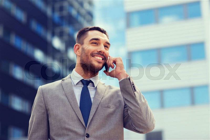 Business, technology and people concept - smiling businessman with smartphone talking over office building, stock photo
