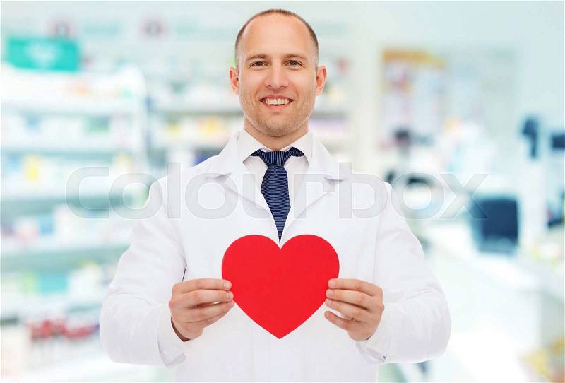 Medicine, pharmacy, people, health care and pharmacology concept - happy male pharmacist holding red heart shape over drugstore background, stock photo