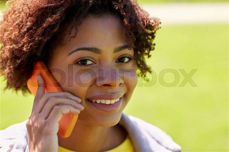 People, technology and leisure concept - happy african american young woman calling on smartphone outdoors, stock photo