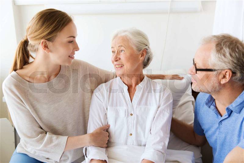 Medicine, support, family health care and people concept - happy senior man and young woman visiting and cheering her grandmother lying in bed at hospital ward, stock photo