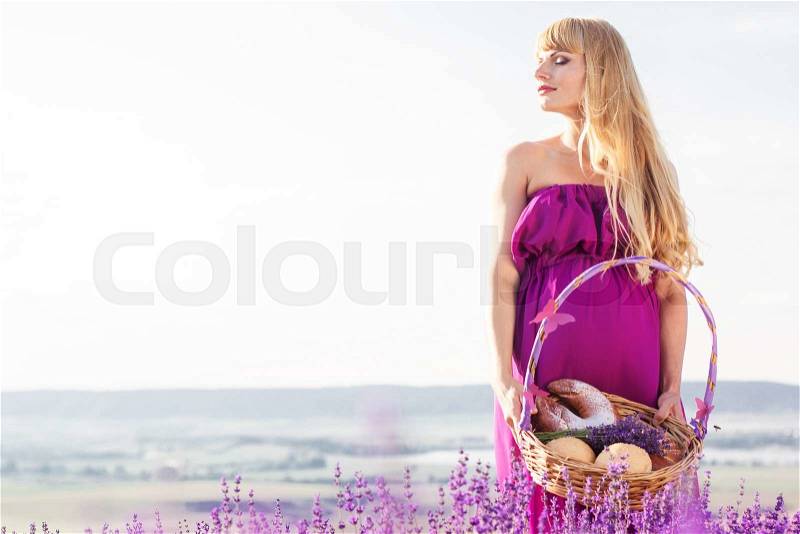 Beautiful pregnant blonde woman is wearing purple dress is holding basket with sweet buns, stock photo