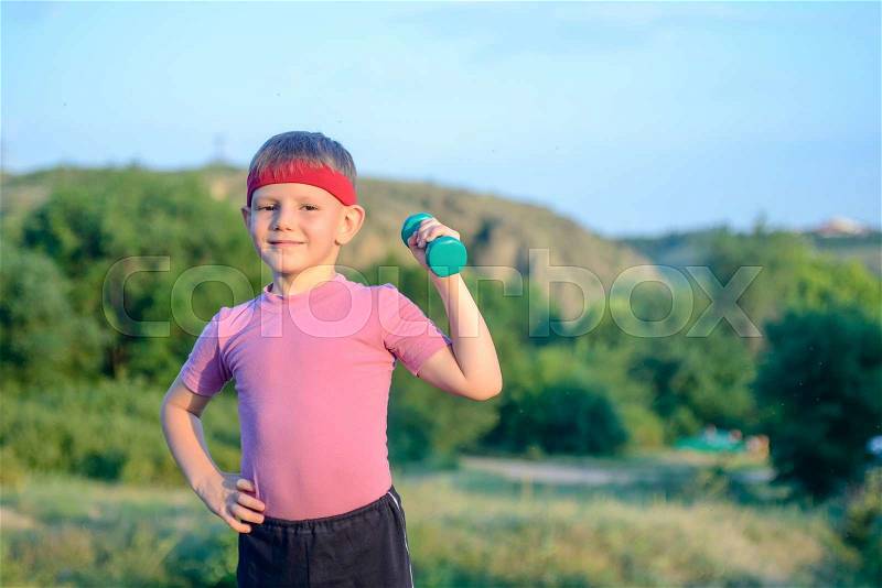 Smiling Strong Cute Boy Lifting Dumbbell with his Right Hand on his Waist While Doing an Outdoor Exercise, stock photo