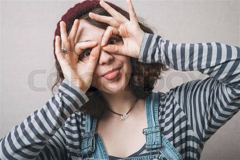 Young happy woman holding her hands over her eyes as glasses and looking through fingers, stock photo