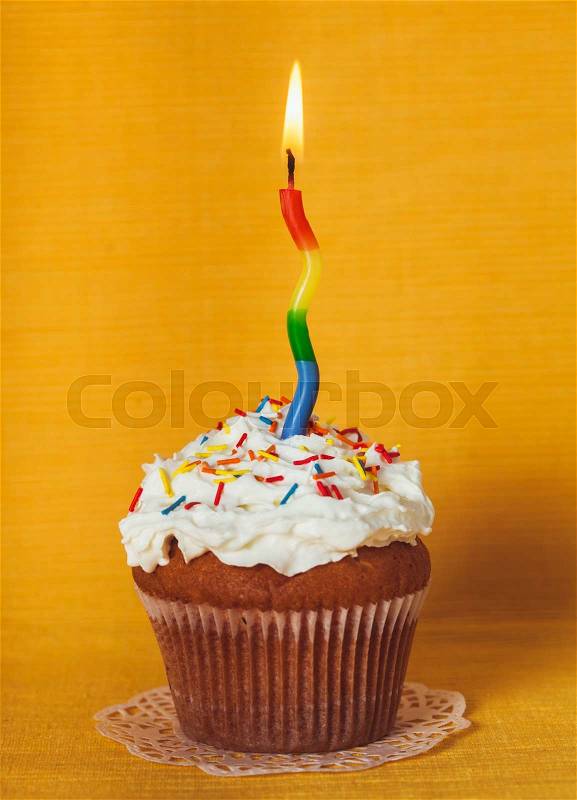 Cupcake with one burning candle on yellow napkin, stock photo