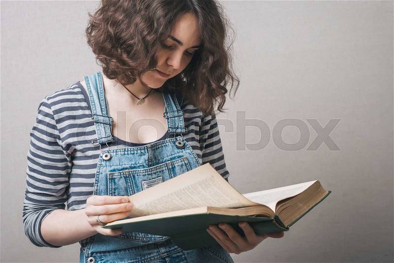 Girl with big book in hand in hand on a gray background, stock photo