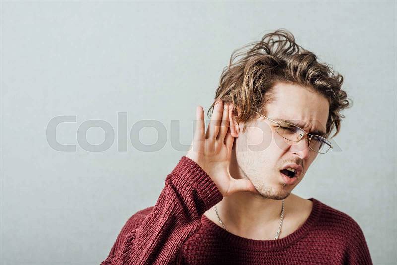 A man with his hand near his ear. Gesture can not hear without listening, talking louder. On a gray background, stock photo