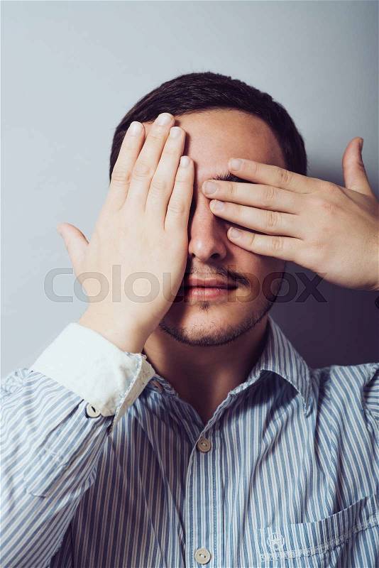 Young man closes his eyes with his hands, stock photo