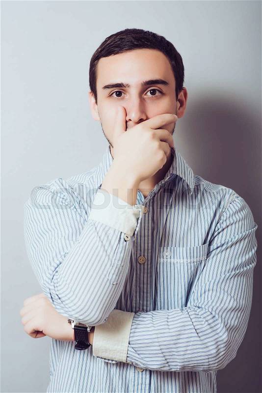 Young handsome man covered her mouth in surprise. Gesture. On a gray background, stock photo