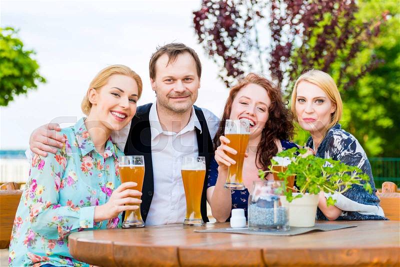 Friends toasting with beer in garden restaurant, stock photo