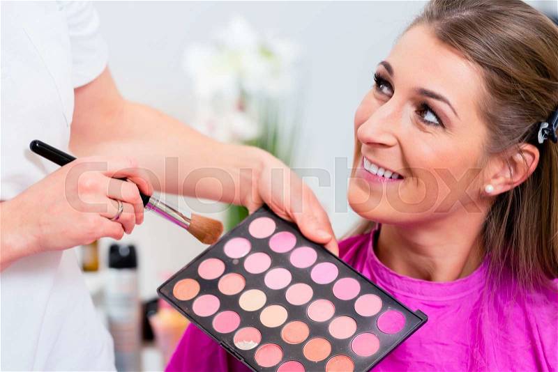 Woman with beautician in cosmetic salon receiving makeup, stock photo