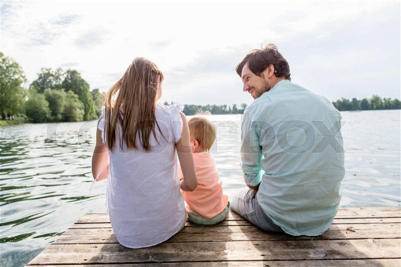 Family sitting on jetty of pond or lake in summer, stock photo