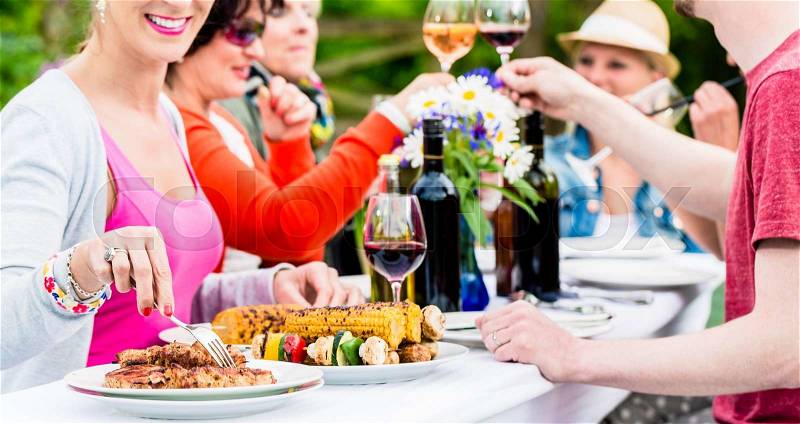 Women and men celebrating garden party, eating and drinking together, stock photo