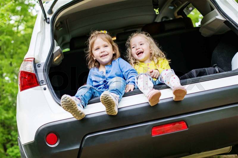 Laughing toddler girls sitting in the car in the forest, stock photo