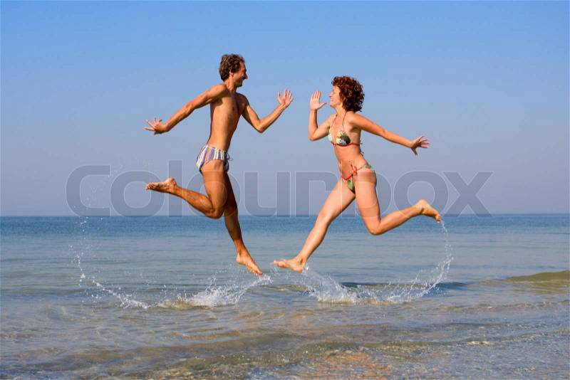 Smiling man and girl jumping at sea shoal with splashes, stock photo