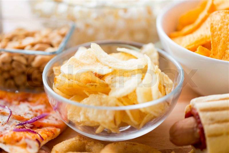 Fast food, junk-food, cuisine and eating concept - close up of crunchy potato crisps in glass bowl and other snacks, stock photo