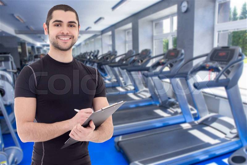 Handsome trainer in sportswear with clipboard in modern gym, stock photo