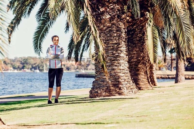 Healthy lifestyle young sporty woman having break between palm trees after jogging at tropical park on sunny summer day, stock photo