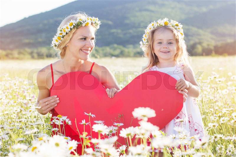Happy family mother with cute little child girl are holding red paper heart in the chamomile field in spring, stock photo