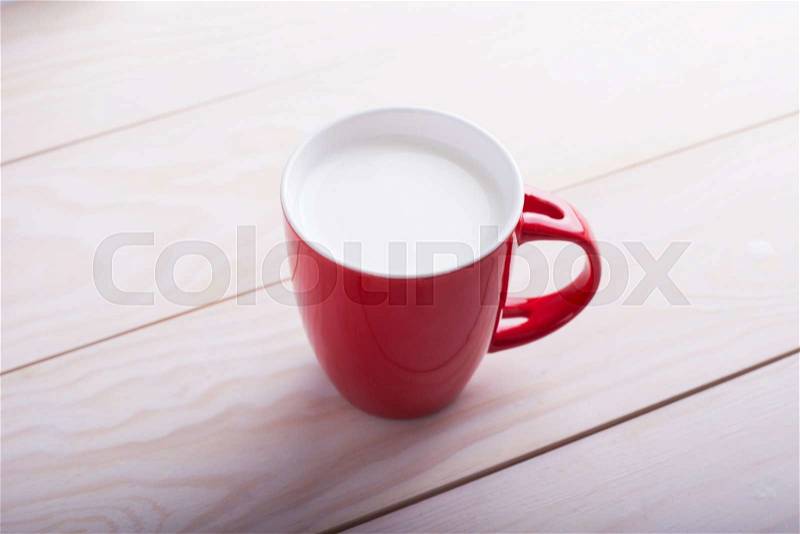 Red cup of milk on wooden table, stock photo