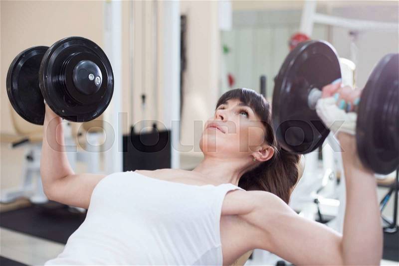 Woman lifting weights and working on her chest at the gym, stock photo