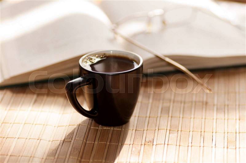 Cup of coffee, standing next to an open book, on which lie glasses, stock photo