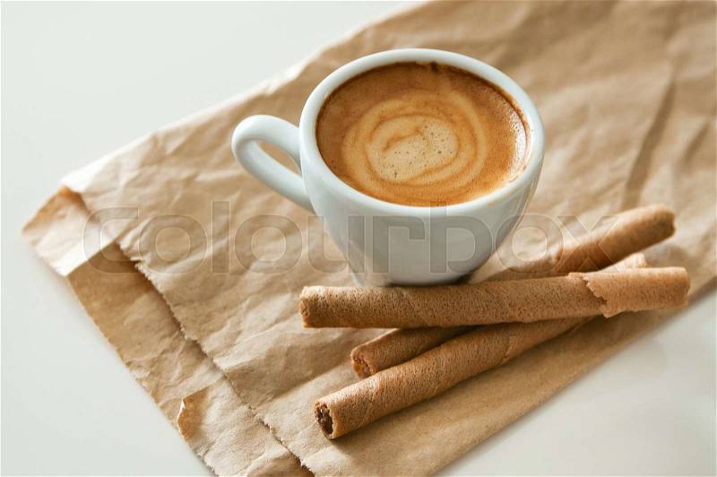 Delicious breakfast cup of strong aroma espresso coffee and chocolate wafer tubes on a recyclable brown paper. Copy space, stock photo