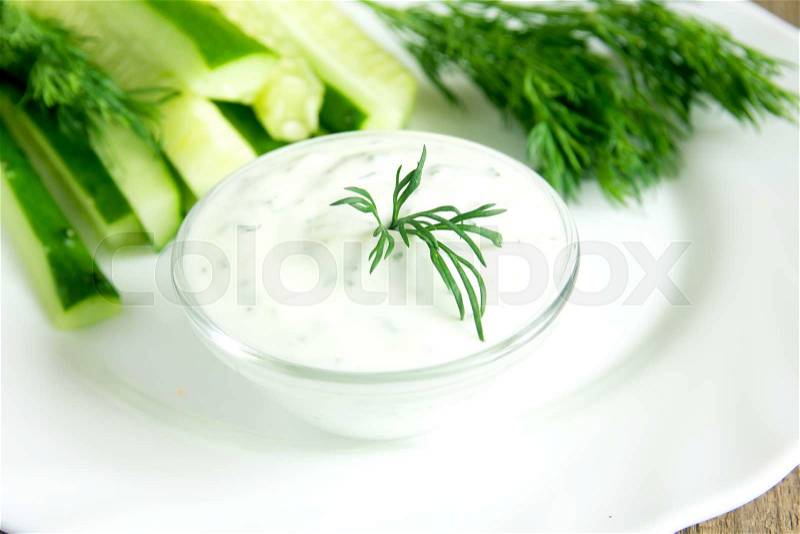 Fresh Greek Tzatziki yogurt dip (sauce) and some ingredients (vegetables) on white plate, horizontal close up, stock photo