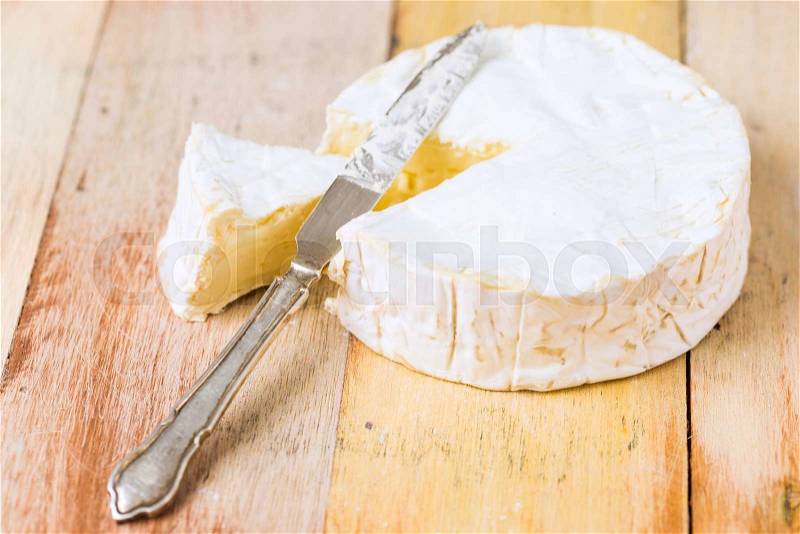 Camembert cheese with cut wedge and vintage knife on wooden table, stock photo