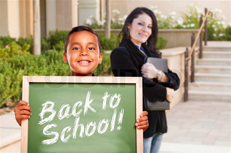 Happy Hispanic Boy Holding Back to School Chalk Board Outside on School Campus as Teacher Looks On, stock photo