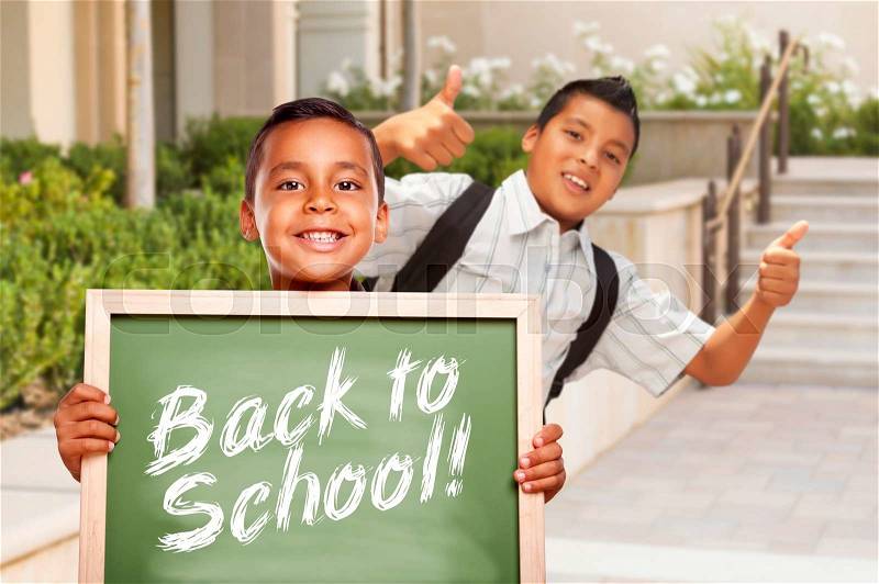 Happy Hispanic Boys Giving Thumbs Up Holding Back to School Chalk Board Outside on School Campus, stock photo
