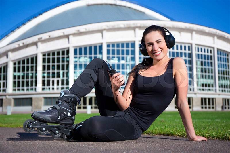 Happy beautiful woman in roller skates sitting and listening music, stock photo