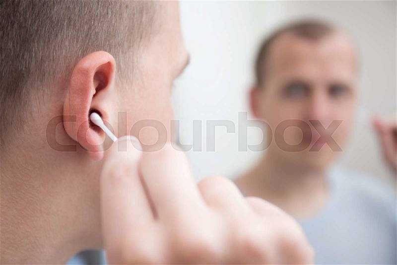 Close up of young man cleaning his ear with a cotton swab, stock photo