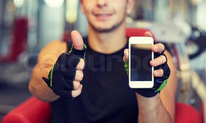Sport, bodybuilding, lifestyle, technology and people concept - happy young man with smartphone showing thumbs up in gym, stock photo