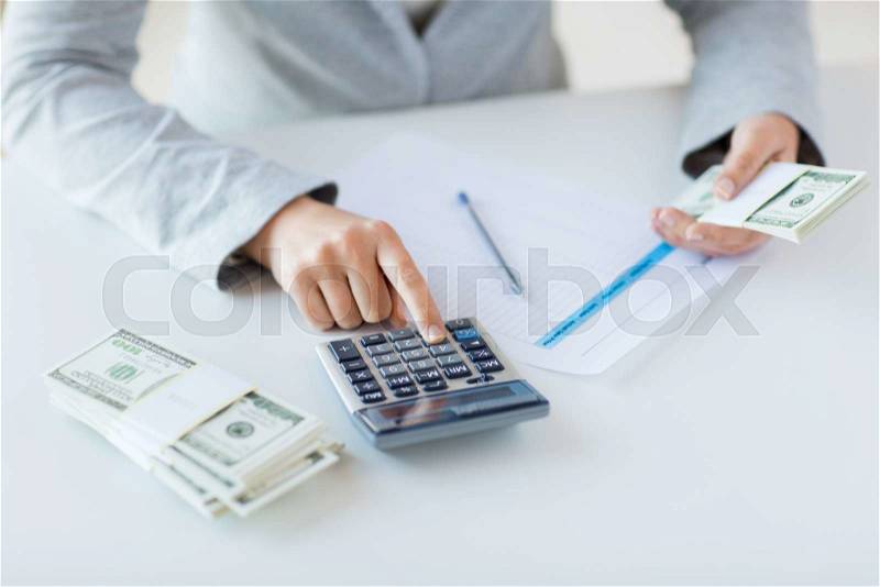 Business, finance, tax and people concept - close up of woman hands counting us dollar money with calculator, stock photo
