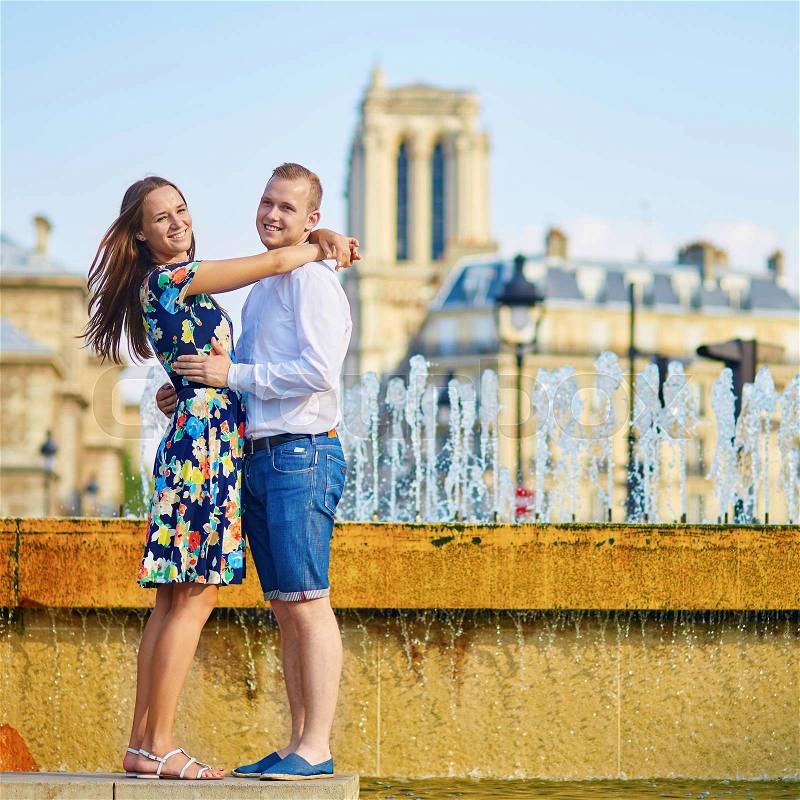 Romantic couple having fun together near the fountain on a hot summer day in Paris. Notre-Dame cathedral is in the background, stock photo