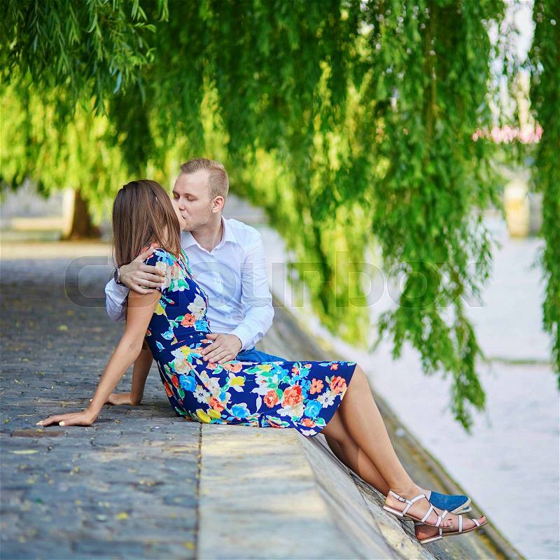 Romantic couple sitting on the Seine embankment on a hot summer day in Paris, stock photo