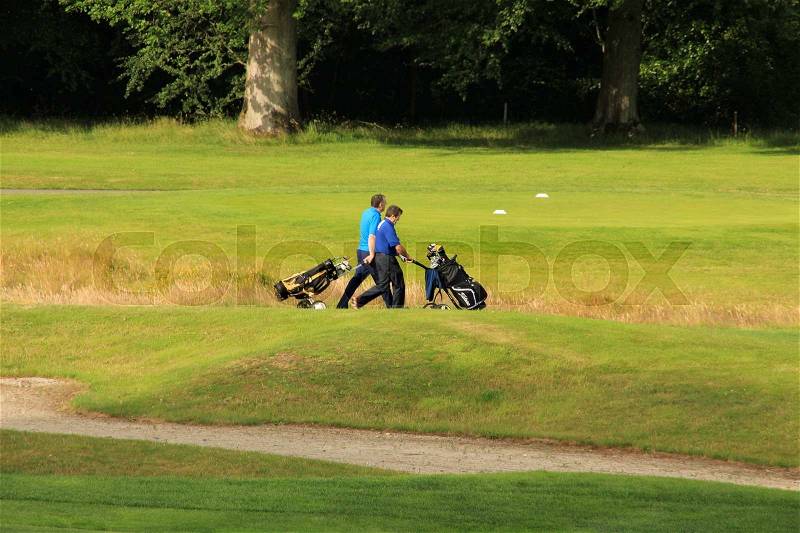 Two men with golf equipment walk over the golf court for playing a match in the summer, stock photo