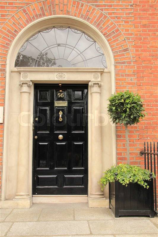 Striking black front door and a potted small tree with vegetation in one of the famous streets in the city Dublin in Ireland in the summer, stock photo