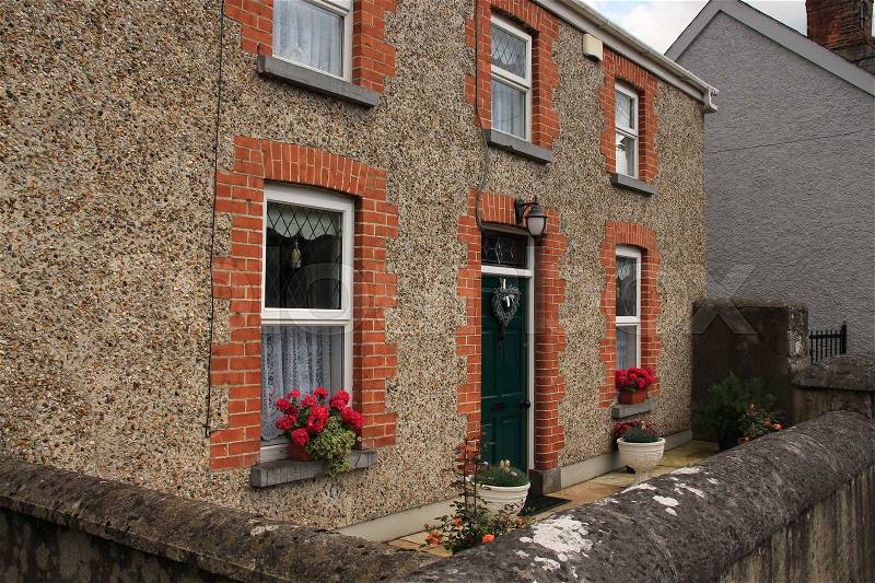 Terraced house with a striking green front door and window boxes with blooming flowers in the residential area in the town Cahir in Ireland in the summer, stock photo