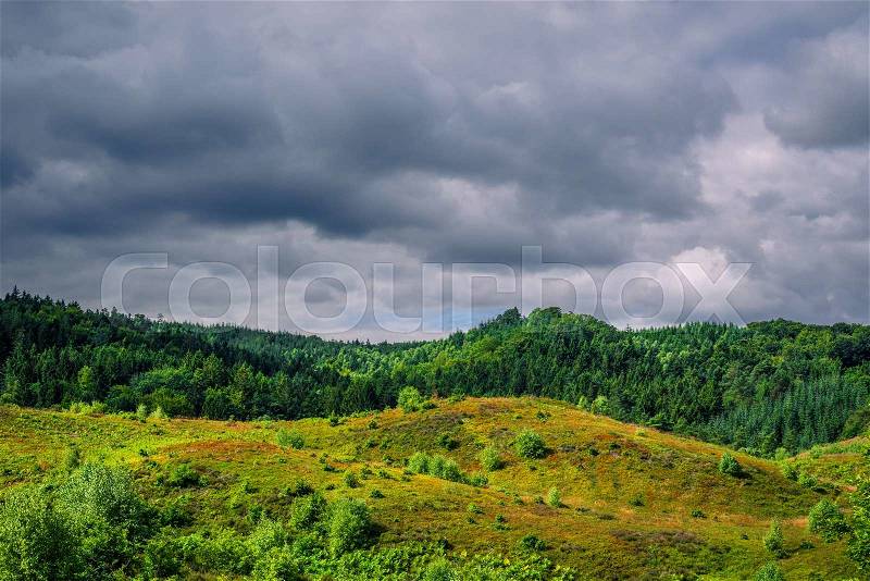 Dark clouds hanging over green nature in Denmark, stock photo