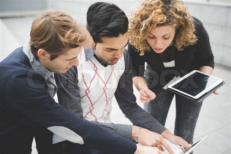 Multiracial contemporary business people working outdoor in town connected with technological devices like tablet and laptop, looking down the screen - finance, business, technology concept, stock photo