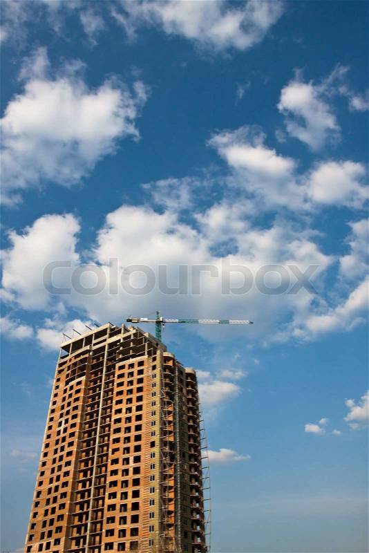 Building under construction with crane, blue sky with clouds, stock photo