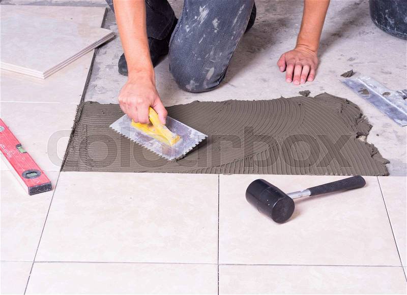 Tiler installing ceramic tiles on a floor, stock photo