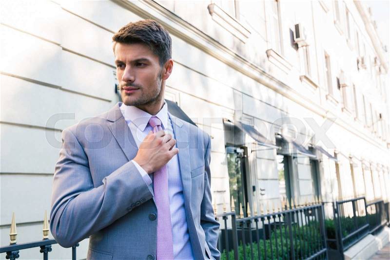 Confident businessman straightens his tie outdoors, stock photo