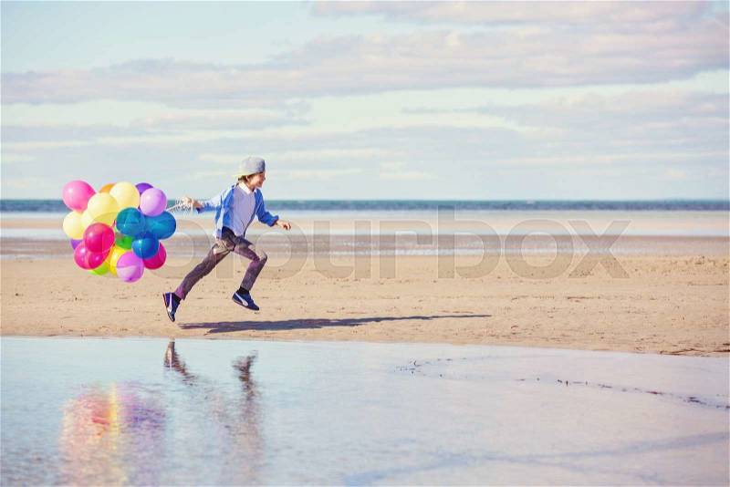 Happy boy plays with colored balloons on the beach having great holidays time on summer. Lifestyle, vacation, happiness, joy concept, stock photo