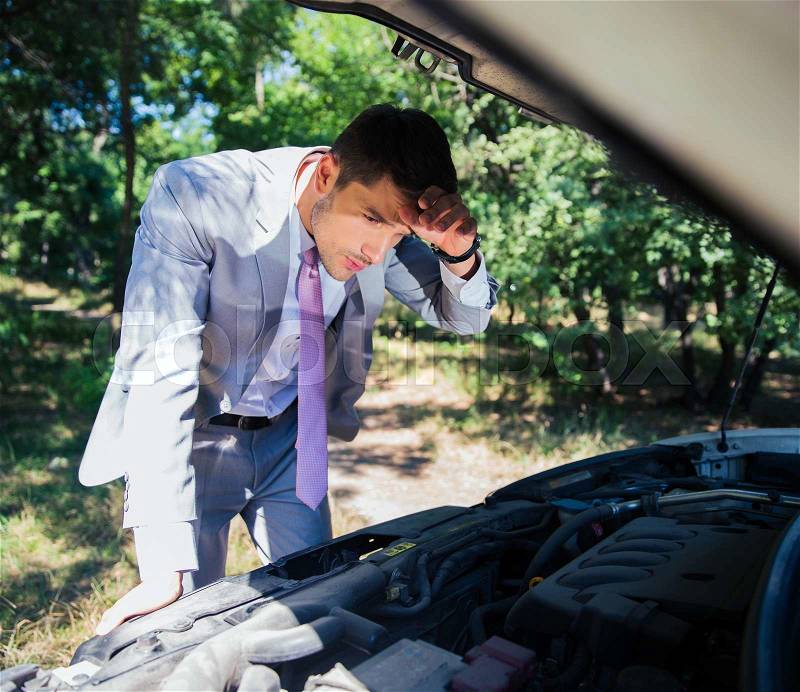 Businessman looking under the hood of breakdown car in forest, stock photo