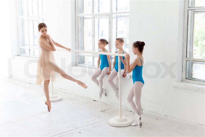 Three little ballerinas with personal ballet teacher in dance studio. classic ballet dancer as teacher posing on one leg at ballet barre on a white background, stock photo