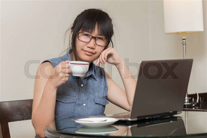 Asian Woman wearing glasses sitting on chair at home and she works on a laptop, stock photo